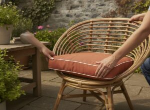 Hands fitting a terracotta replacement cushion onto a rattan wicker armchair on a garden terrace