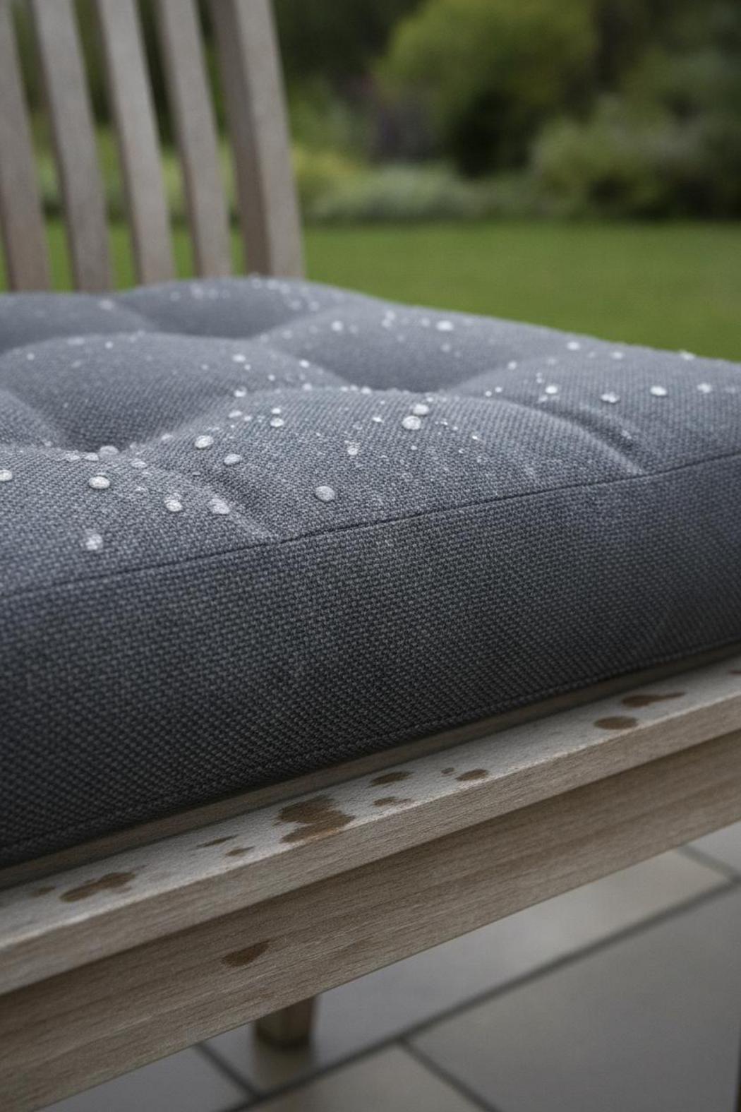 Raindrops beading on textured Sunbrella fabric of one of the best bench cushions for outdoor use on a teak garden bench