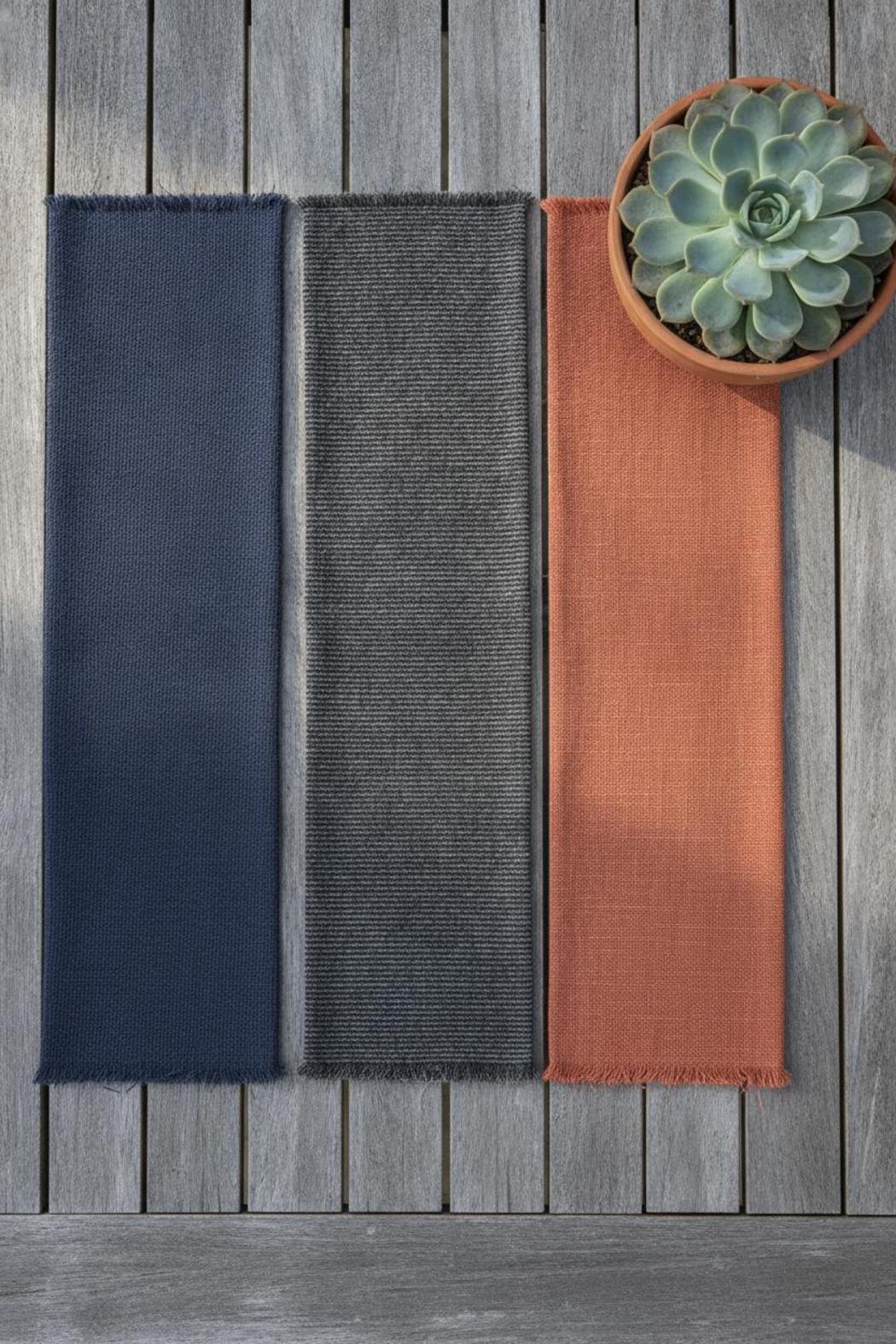Three fabric swatches for best outdoor cushions for patio furniture in navy, grey, and terracotta on weathered teak table with succulent