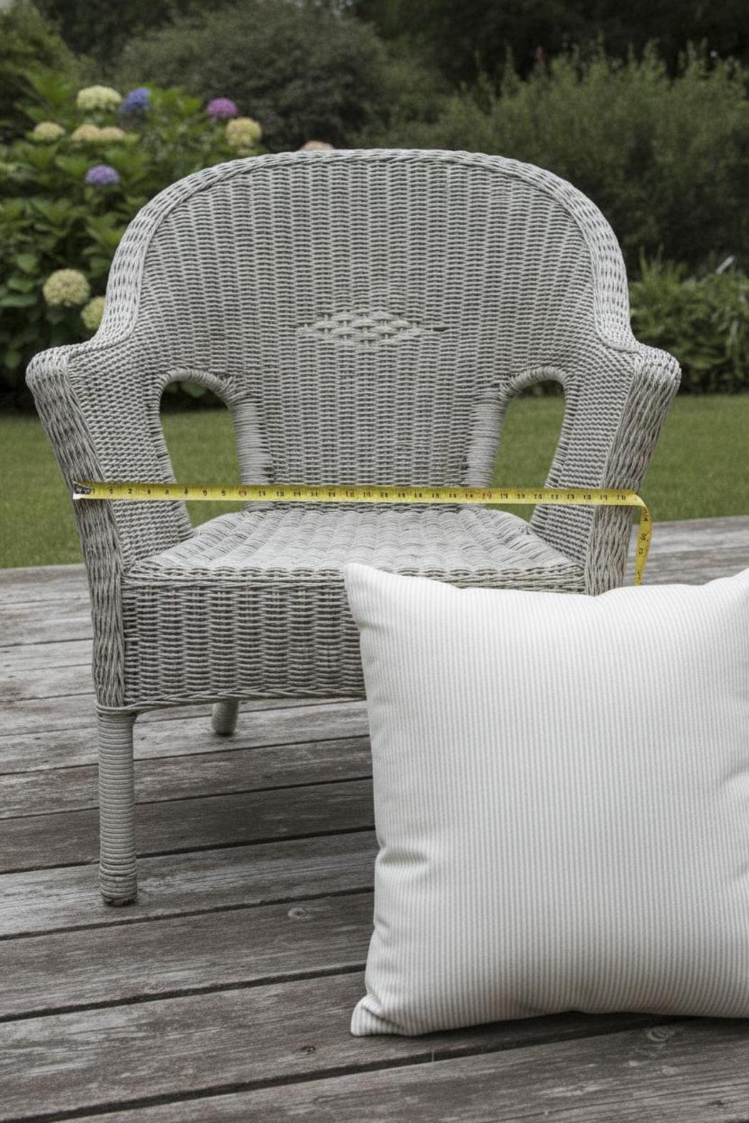 Measuring a wicker armchair on a wooden deck for replacement cushions for outdoor furniture beside it