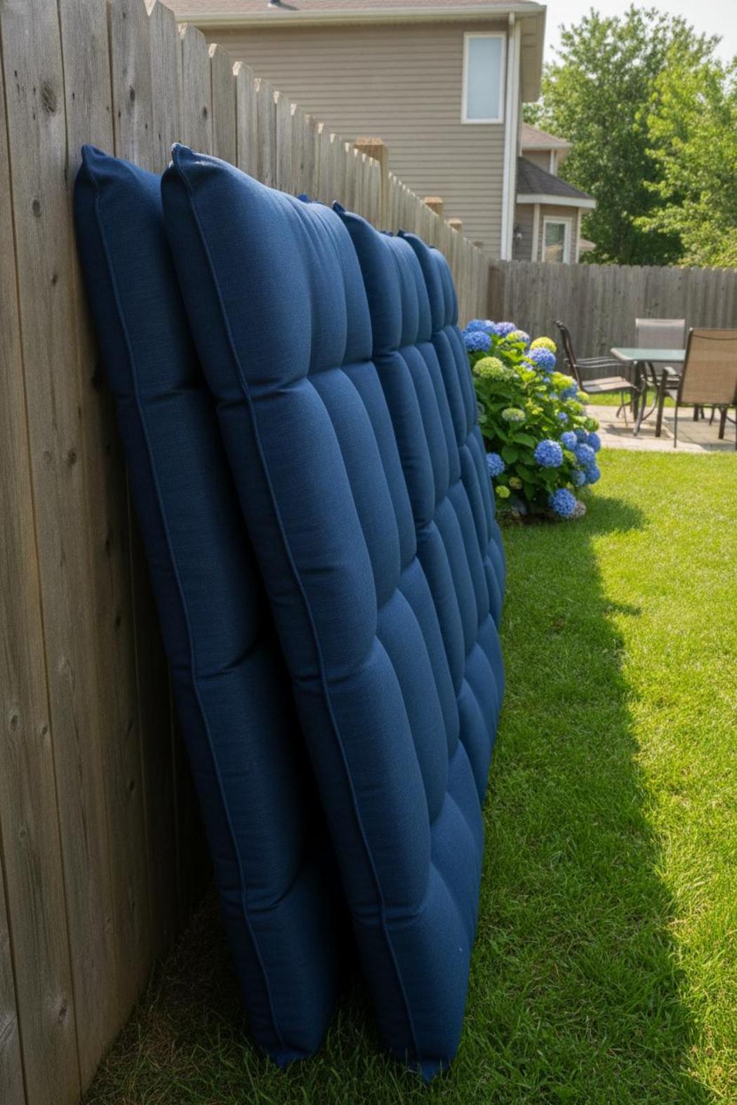 Navy blue outdoor patio cushions air drying upright against a cedar fence in bright summer sunlight